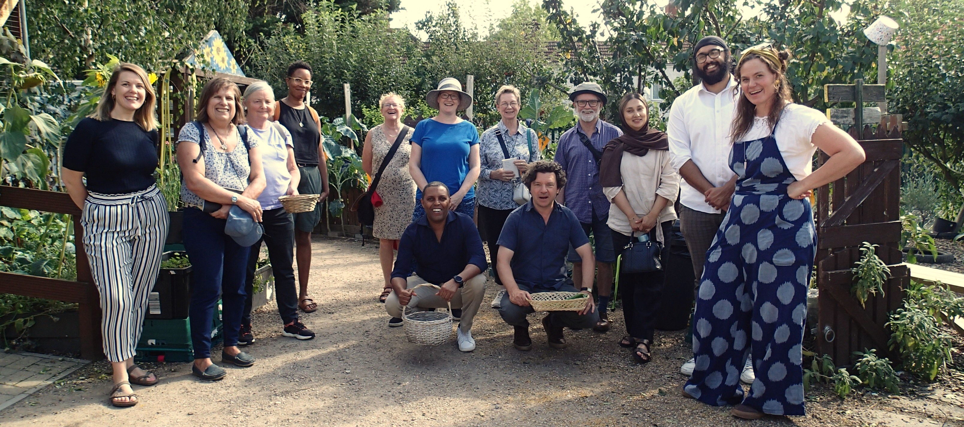 A group of a dozen people stand in a community garden and smile for the camera