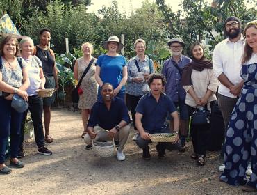 A group of a dozen people stand in a community garden and smile for the camera